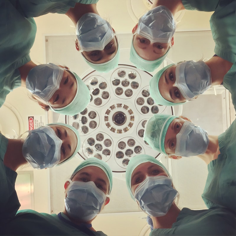 Overhead view of a dental team in masks and caps gathered around an operatory light