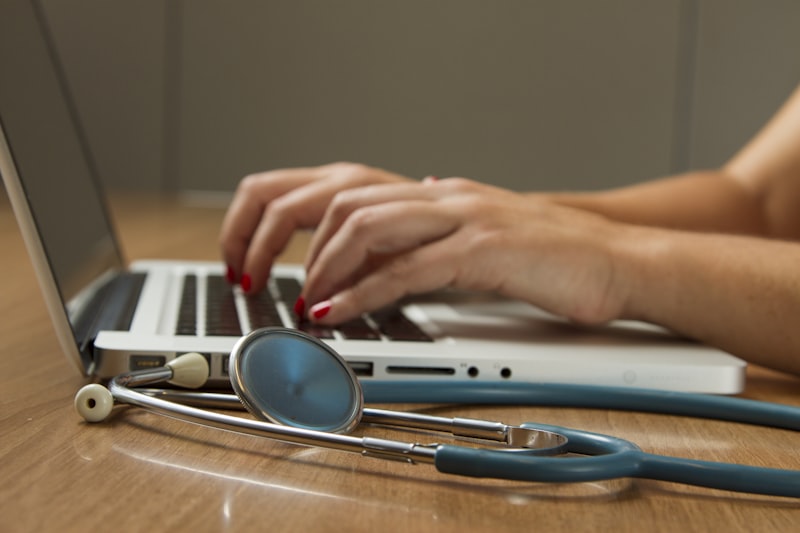 Healthcare professional working at a laptop with a stethoscope resting on the desk
